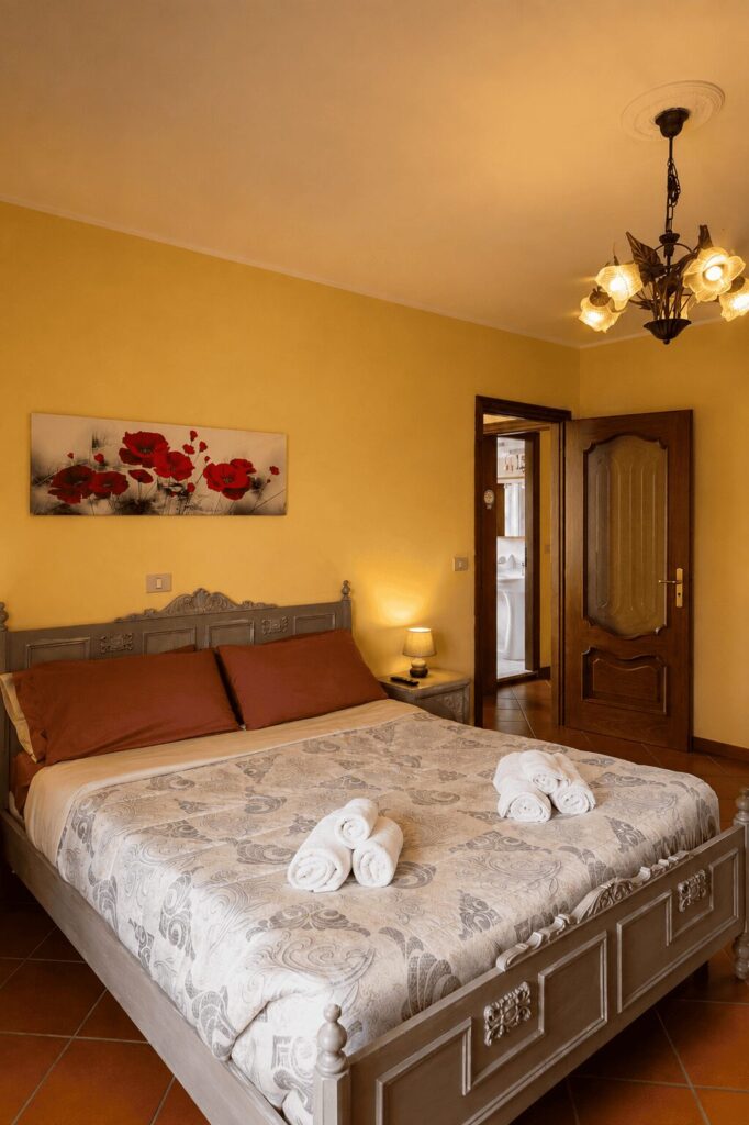 Letto matrimoniale con testiera intagliata e abat-jour accesa, con la porta aperta verso il bagno