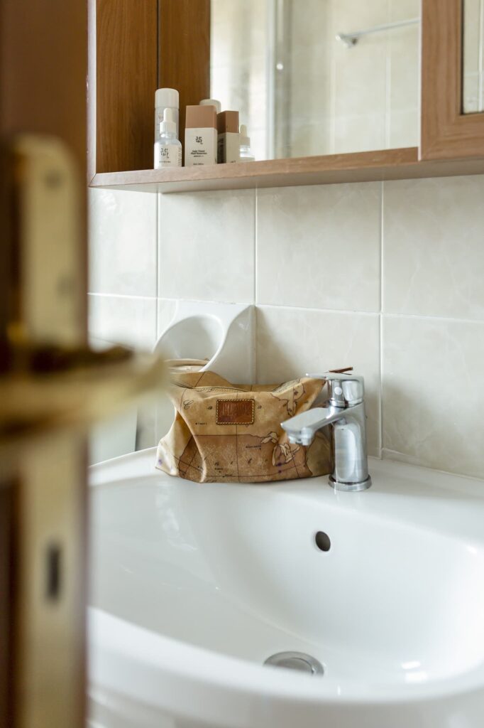 Dettaglio del lavabo in ceramica con rubinetto cromato, beauty case e set di cortesia sulla mensola