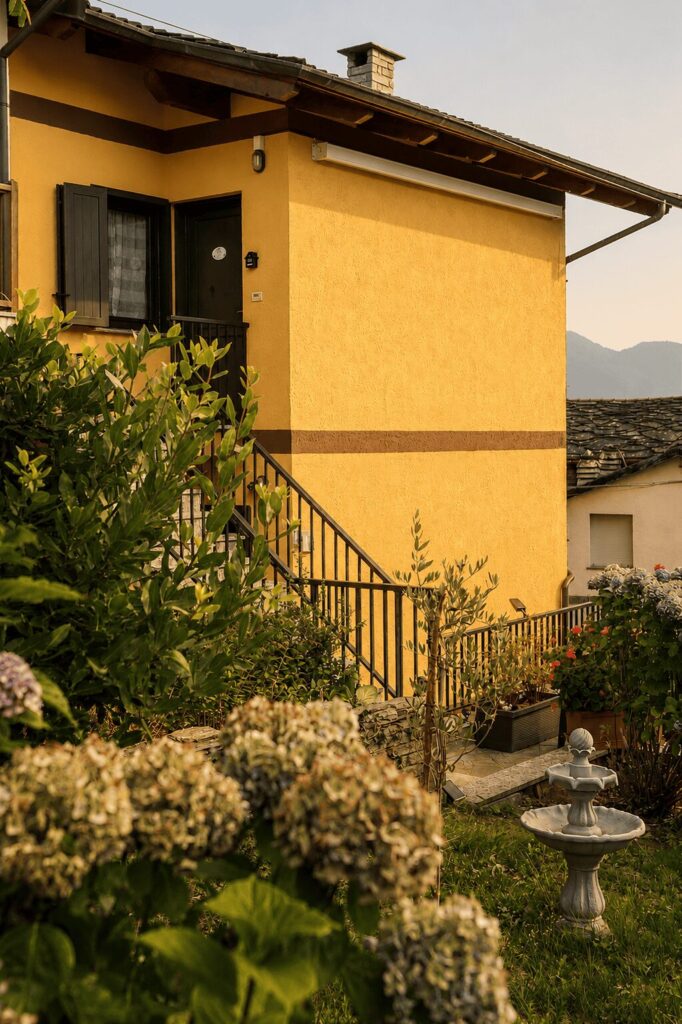 La facciata gialla del Sunrise Inn al tramonto, con scala esterna, ortensie fiorite e le montagne sullo sfondo