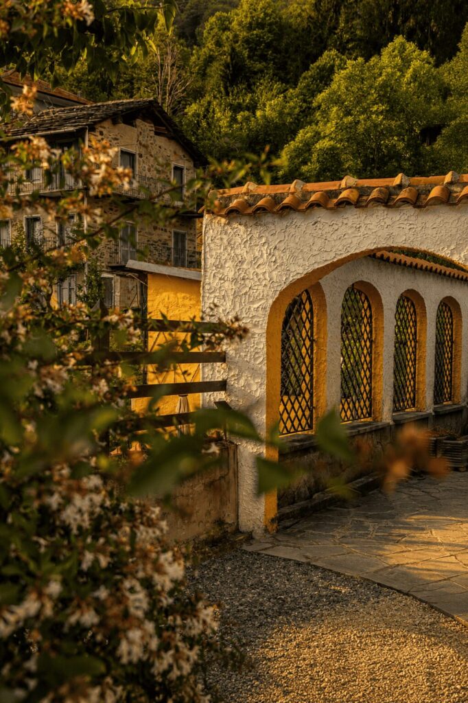 Loggiato ad archi gialli con grate a rombi, tetto in coppi e le case in pietra della borgata tra il verde del bosco