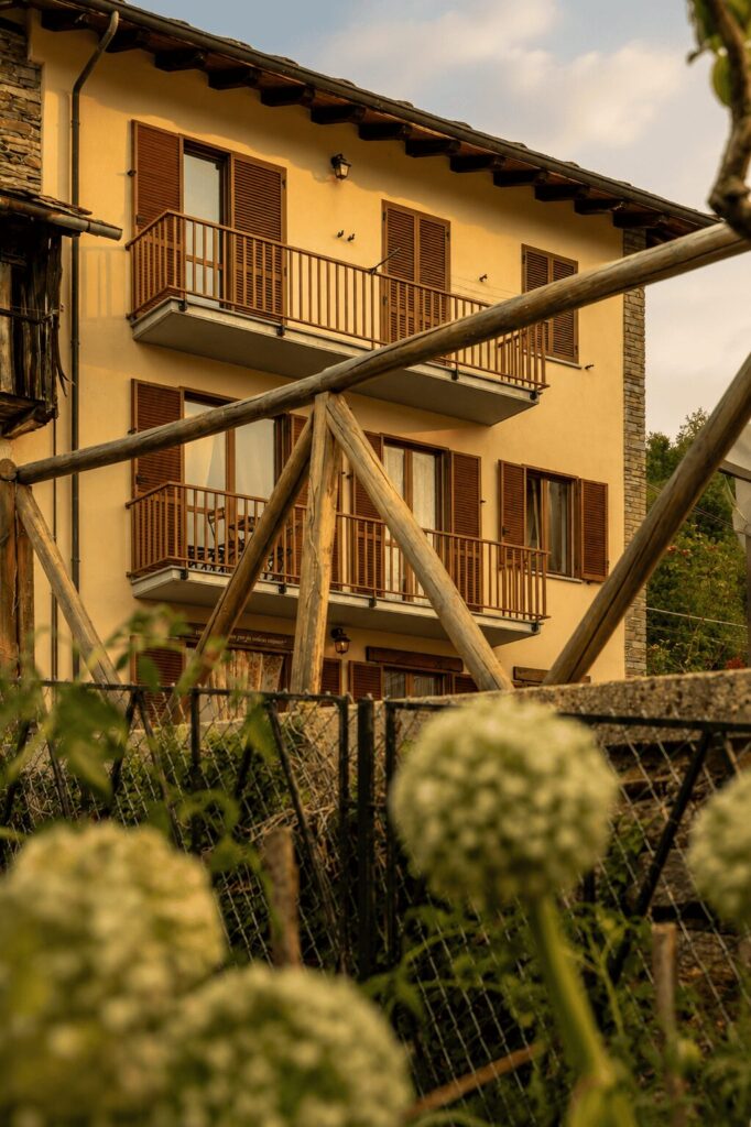 Balconi in legno e persiane a doghe sulla facciata color crema, visti da un prato con fiori bianchi