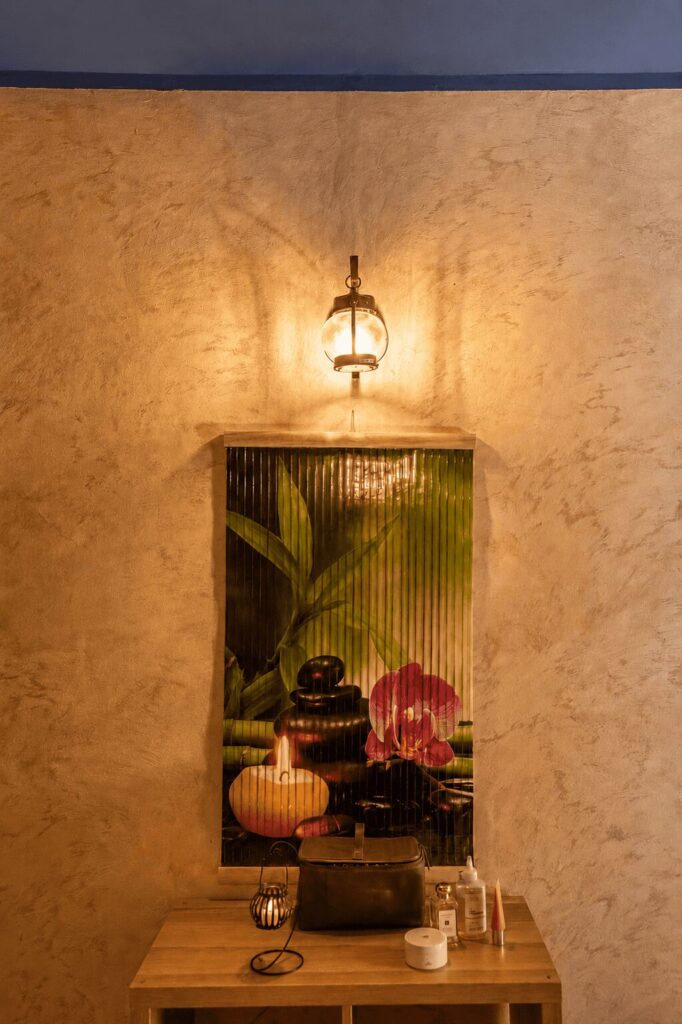 Angolo della spa con parete in stucco color sabbia, lanterna accesa e quadro zen con orchidea e bambù