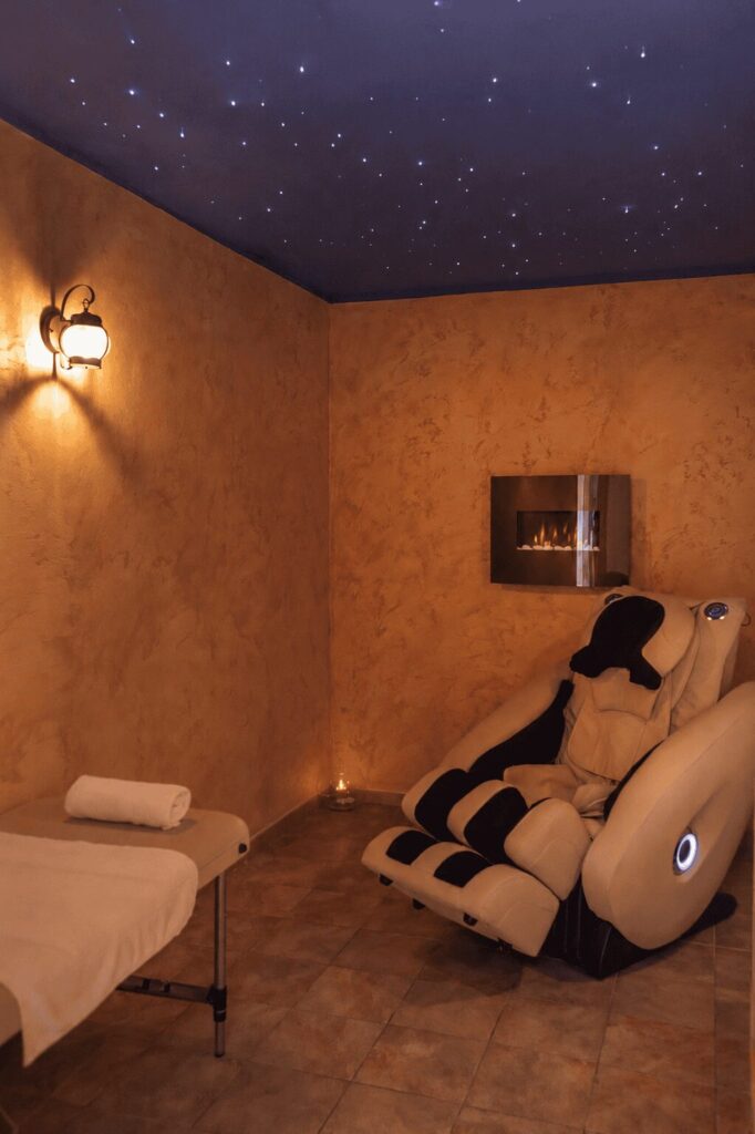 Sala relax con lettino da massaggio, poltrona massaggiante, camino a parete e soffitto stellato blu