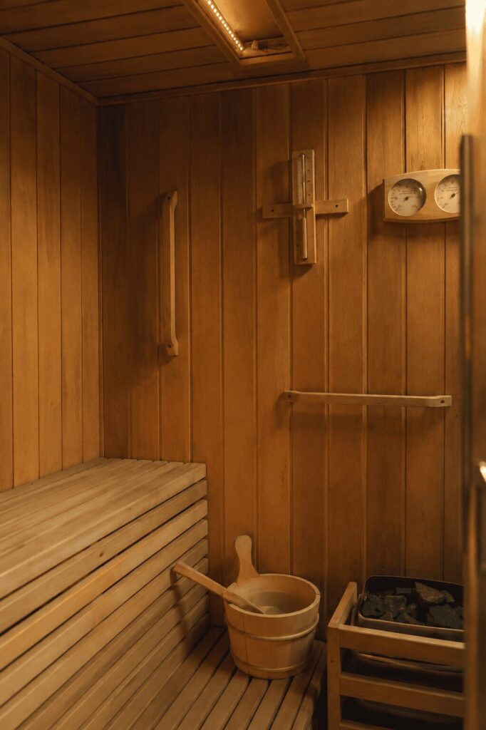 Interno della sauna finlandese in legno con panche, secchio e mestolo e stufa con pietre laviche