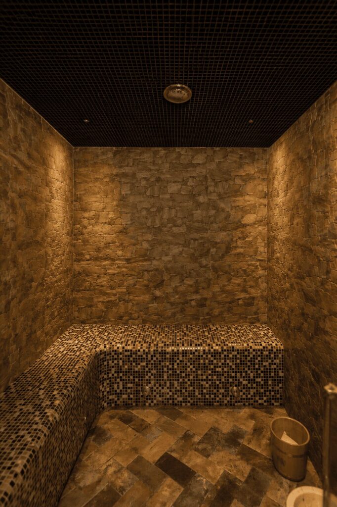 Bagno turco con pareti in pietra, panca rivestita di mosaico scuro e luce calda radente